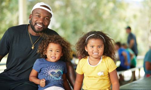 father with his two daughters smiling at a picnic table