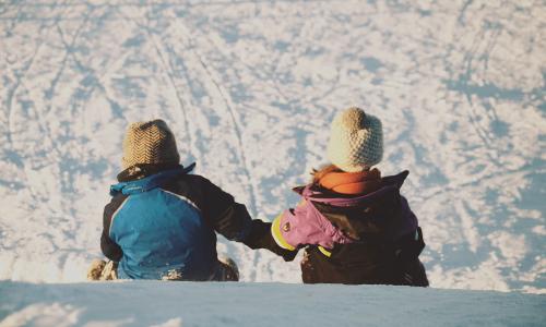 2 kids sledding and holding hands