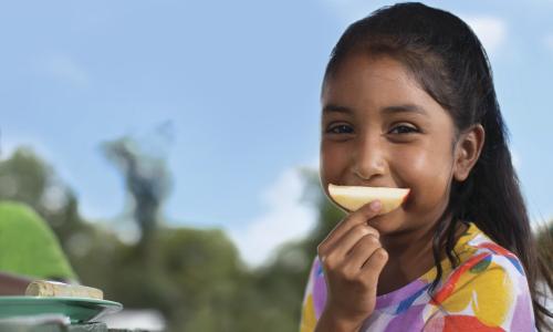 girl with an apple slice over mouth like a smile