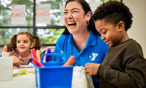 Childcare staff member (Female) laughing with 2 kids doing crafts