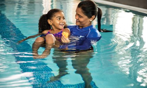 Staff person helping young girl float in the pool