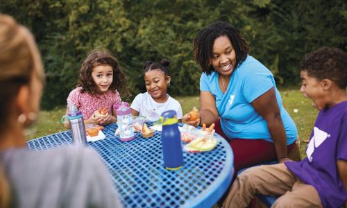 Campers and counselor at lunch table outside