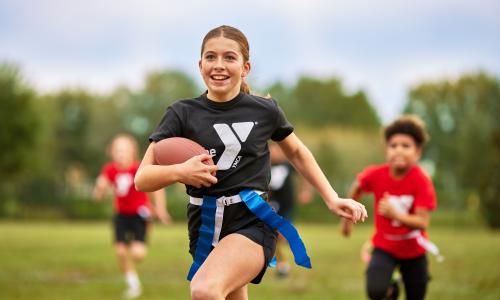 Girl playing flag football runs toward the camera excitedly