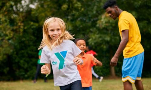 Child runs with friends while YMCA camp counselor monitors