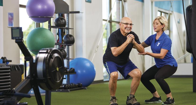 YMCA staff member assisting an older adult with fitness training in a YMCA facility.
