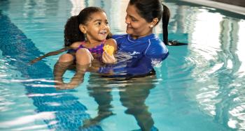 Staff person helping young girl float in the pool