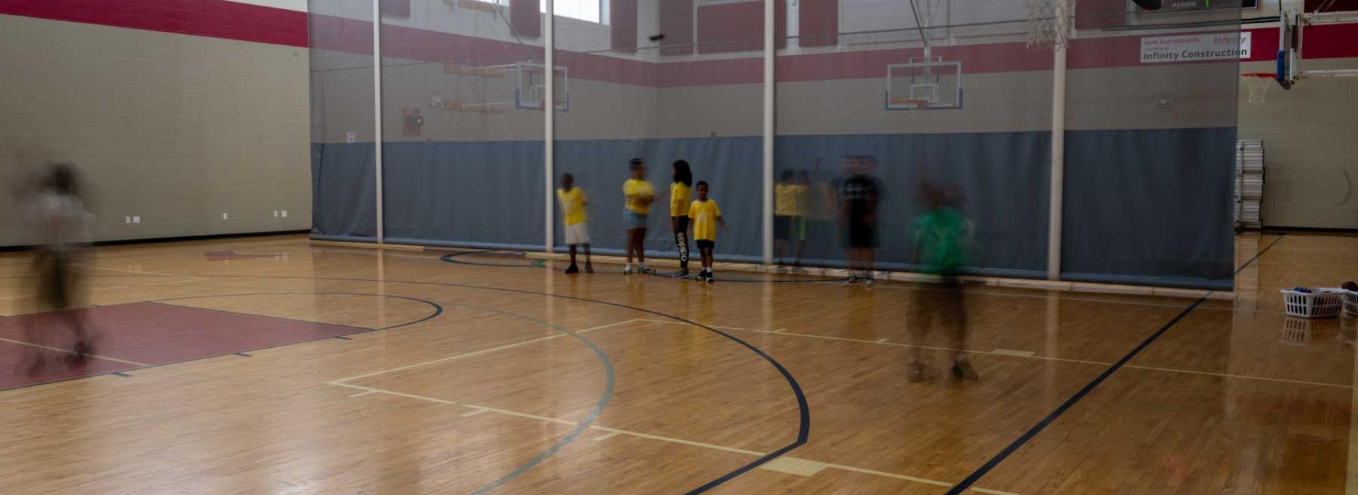 Image shows basketball court with a semi-permanent wall with campers playing basketball.