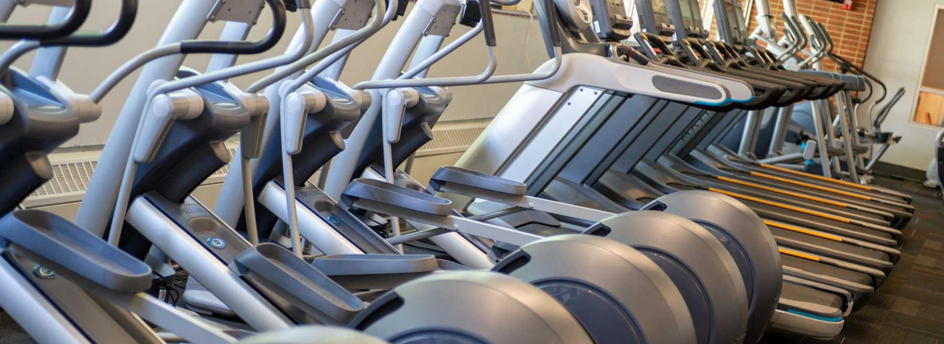 Image shows cardio machines in a line. TVs placed throughout workout facility.