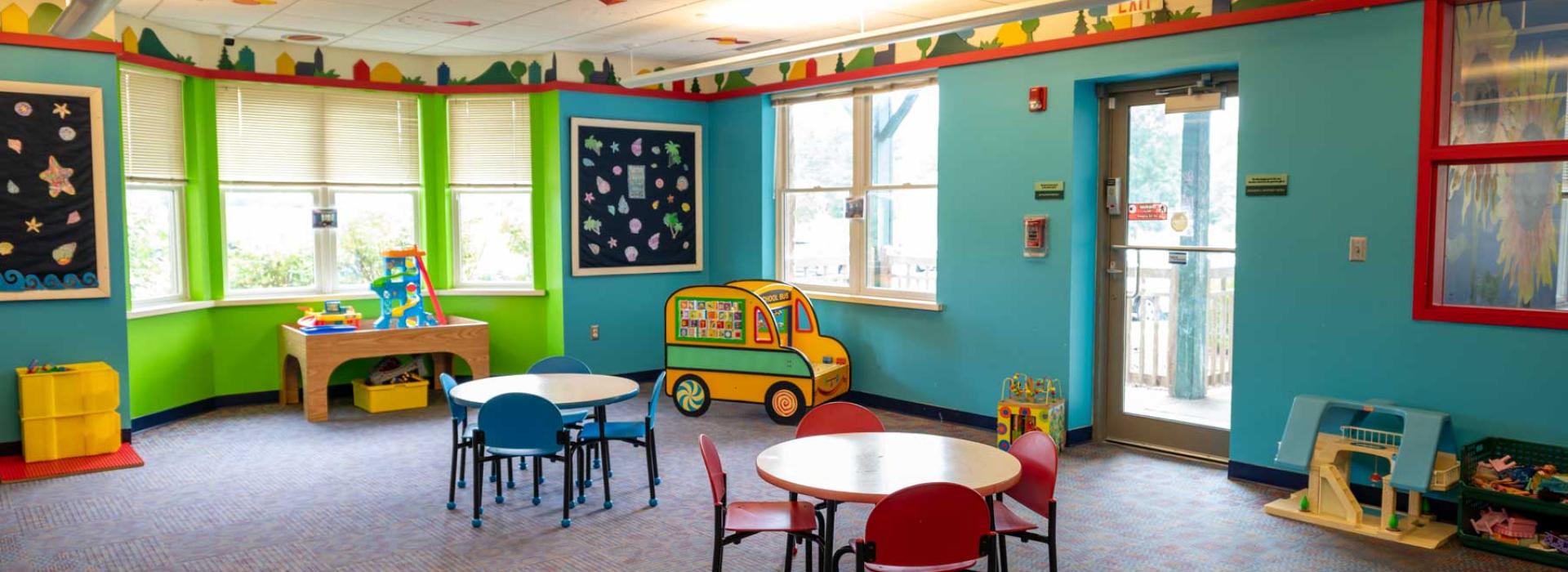 One of the Child Watch areas at the Geauga YMCA. Image shows kid's tables and chairs, toys, pretend school bus, and child-life atmosphere.